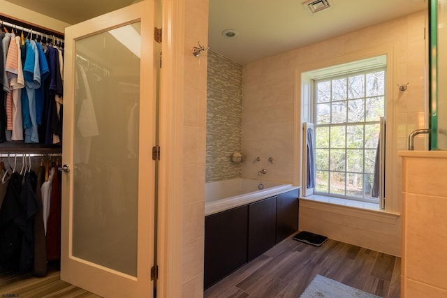 bathroom with visible vents, a bath, wood finished floors, and a spacious closet