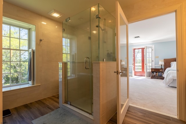 ensuite bathroom featuring plenty of natural light, a stall shower, ensuite bath, and wood finished floors
