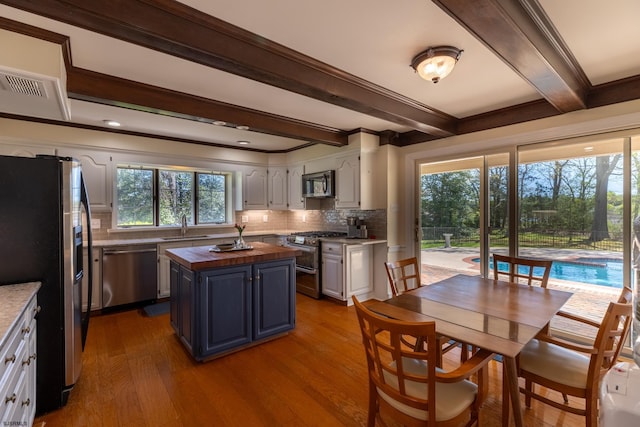 kitchen featuring stainless steel appliances, butcher block countertops, decorative backsplash, and beam ceiling