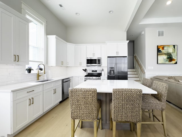 kitchen with a sink, light wood-style floors, stainless steel appliances, white cabinetry, and visible vents