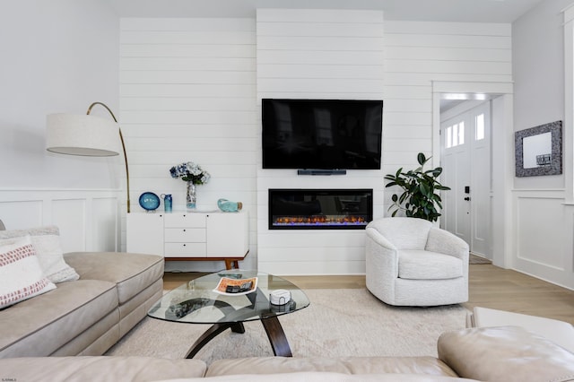 living area featuring a glass covered fireplace, wood finished floors, and a decorative wall