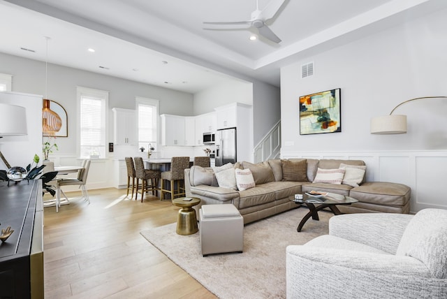 living room with visible vents, stairs, ceiling fan, and a decorative wall
