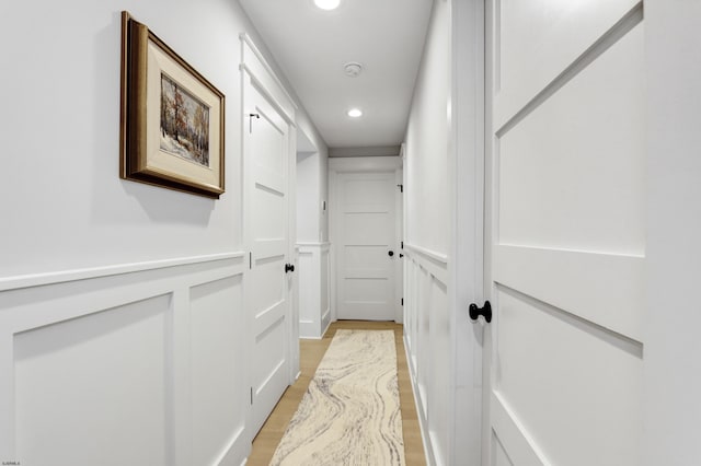 hall featuring a decorative wall, recessed lighting, a wainscoted wall, and light wood-type flooring