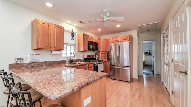 kitchen featuring a ceiling fan, a kitchen bar, a sink, light wood-style flooring, and stainless steel appliances