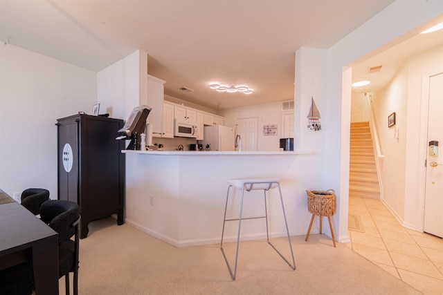 kitchen featuring baseboards, a breakfast bar, white cabinets, and white appliances