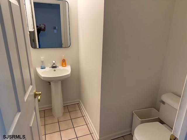 half bathroom featuring baseboards, tile patterned flooring, and toilet