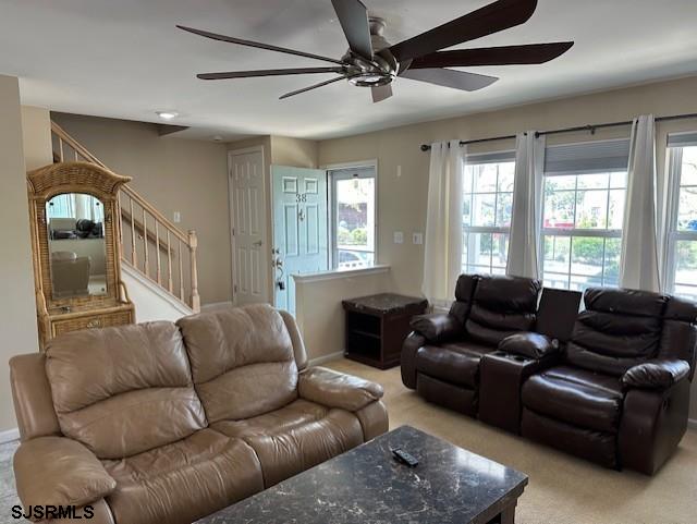 living room with baseboards, ceiling fan, stairs, and light colored carpet