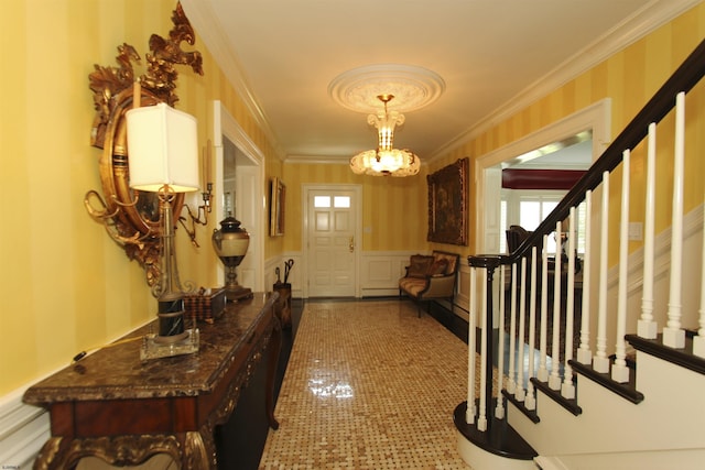 foyer entrance with wainscoting, a chandelier, ornamental molding, a decorative wall, and stairs