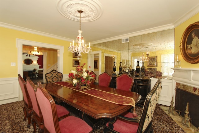 dining room featuring visible vents, a wainscoted wall, a chandelier, ornamental molding, and a decorative wall