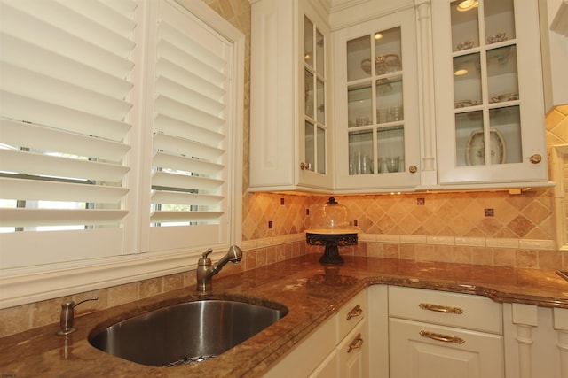kitchen with glass insert cabinets, dark stone counters, white cabinetry, tasteful backsplash, and a sink