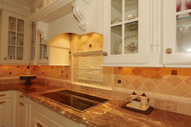 kitchen with decorative backsplash, black electric stovetop, glass insert cabinets, and dark stone countertops