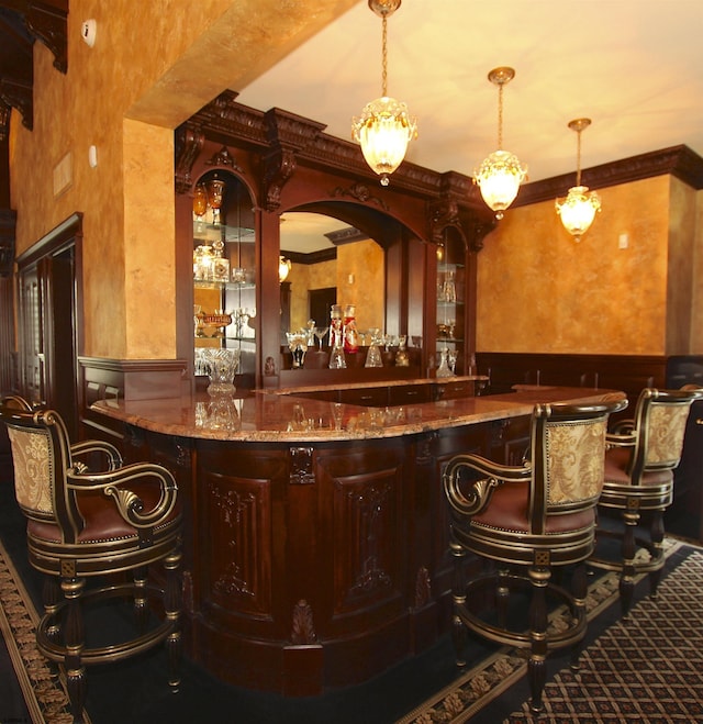 bar featuring a wainscoted wall, ornamental molding, indoor wet bar, and decorative light fixtures