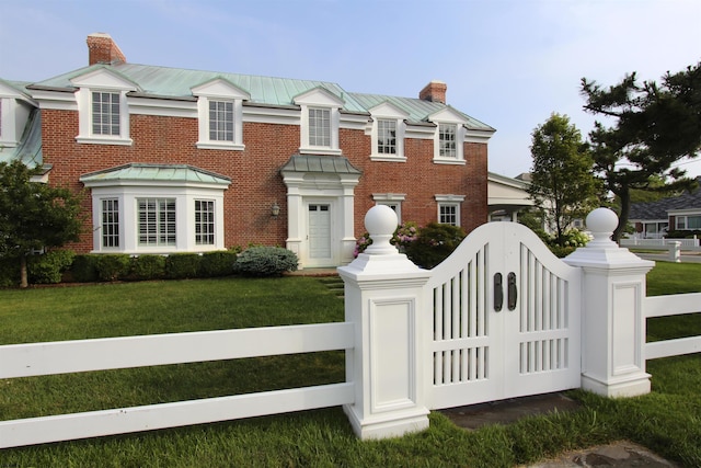 view of front of property with a standing seam roof, a fenced front yard, a chimney, a front yard, and a gate