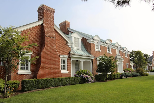 view of property exterior with brick siding, a chimney, a standing seam roof, a yard, and metal roof