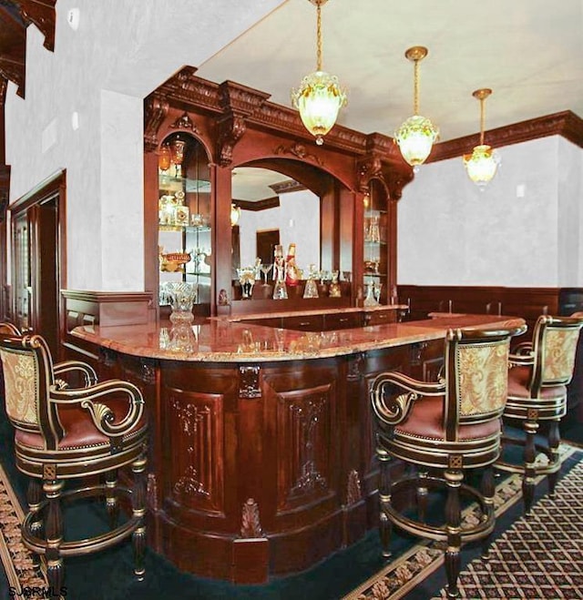 bar featuring crown molding, hanging light fixtures, wainscoting, and wet bar