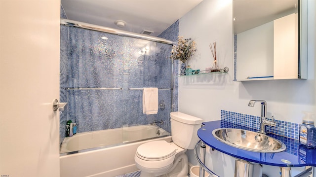 bathroom featuring backsplash, toilet, a sink, and bath / shower combo with glass door