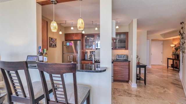 kitchen with a kitchen breakfast bar, dark countertops, a toaster, freestanding refrigerator, and glass insert cabinets