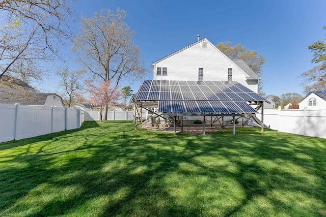 rear view of house featuring a fenced backyard, a yard, and solar panels