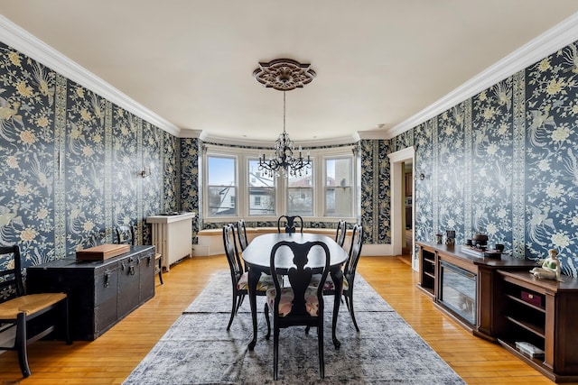 dining space with crown molding, light wood-style flooring, a notable chandelier, and wallpapered walls