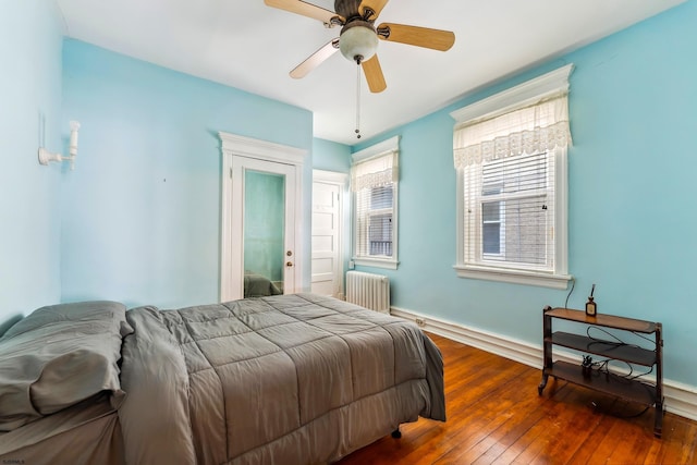 bedroom with baseboards, multiple windows, radiator heating unit, and hardwood / wood-style floors
