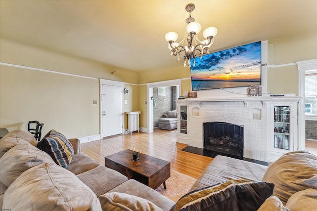 living area with a brick fireplace, baseboards, an inviting chandelier, and wood finished floors