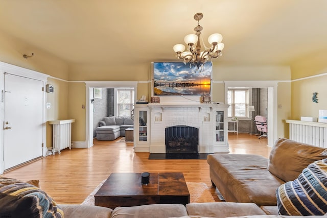 living room with radiator heating unit, a fireplace, light wood-style flooring, and a chandelier