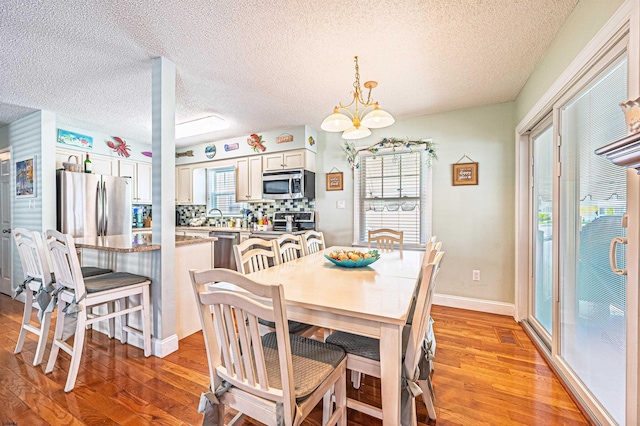 dining area with a textured ceiling, an inviting chandelier, and light wood finished floors