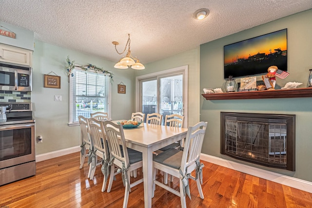 dining space featuring a glass covered fireplace, a textured ceiling, baseboards, and wood finished floors
