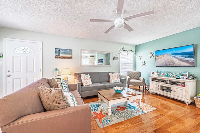 living room with a ceiling fan, light wood finished floors, and a textured ceiling