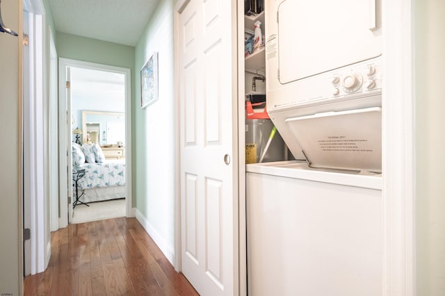 clothes washing area with baseboards, laundry area, stacked washer and dryer, and wood finished floors