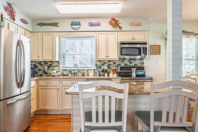 kitchen with a sink, a textured ceiling, appliances with stainless steel finishes, and decorative backsplash