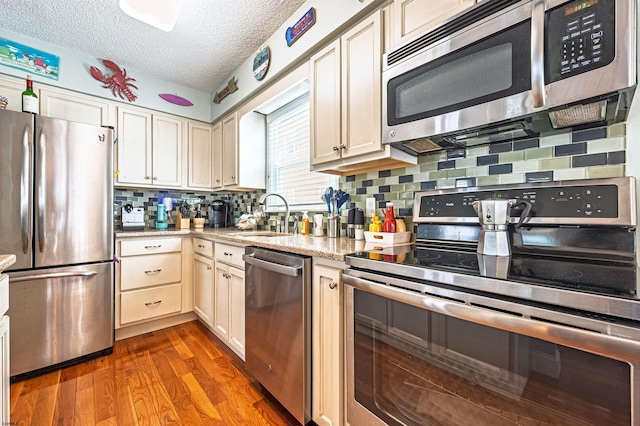 kitchen featuring backsplash, a textured ceiling, a sink, stainless steel appliances, and light wood-style flooring