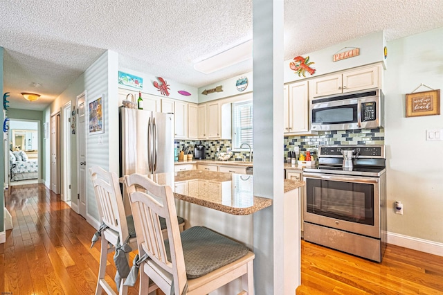 kitchen featuring a textured ceiling, appliances with stainless steel finishes, light wood finished floors, and tasteful backsplash