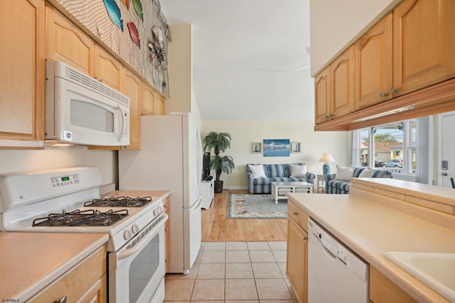 kitchen featuring light brown cabinetry, light countertops, a sink, white appliances, and light tile patterned flooring