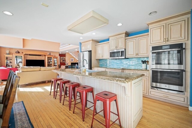 104 Van Sant Ave, Linwood, NJ 08221 - kitchen with cream cabinets, a sink, light wood finished floors, a breakfast bar, and stainless steel appliances
