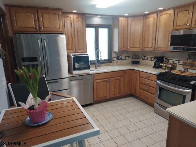 kitchen with light tile patterned flooring, light countertops, brown cabinets, a sink, and stainless steel appliances