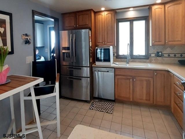 kitchen featuring a sink, appliances with stainless steel finishes, light tile patterned floors, and tasteful backsplash