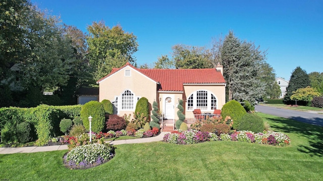 mediterranean / spanish house with a front lawn, stucco siding, a tile roof, and a chimney