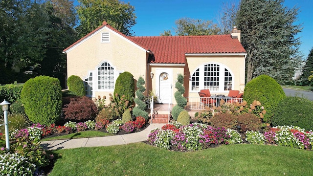 mediterranean / spanish-style house with a tiled roof, a front lawn, stucco siding, and a chimney