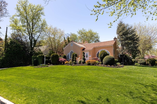 mediterranean / spanish house with a chimney, a tile roof, a front yard, and stucco siding