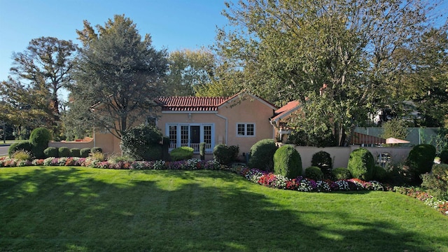 rear view of house featuring a lawn, stucco siding, a tile roof, and fence