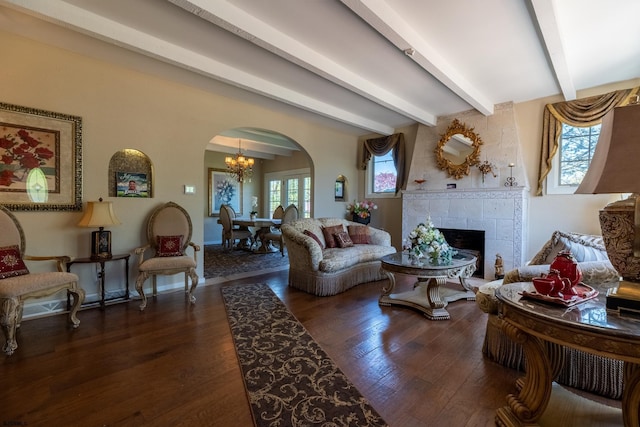 living room featuring arched walkways, a fireplace, dark wood finished floors, beamed ceiling, and an inviting chandelier
