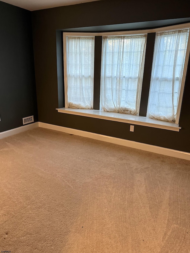 carpeted empty room featuring baseboards and visible vents