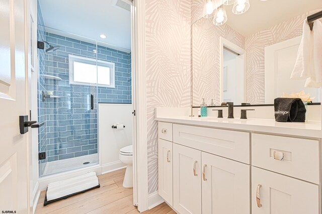 full bath with a stall shower, wood finished floors, vanity, toilet, and a notable chandelier