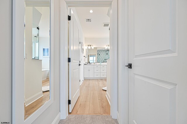 hallway featuring baseboards, visible vents, and light wood finished floors