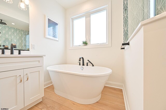 full bath with baseboards, a soaking tub, vanity, and wood finished floors