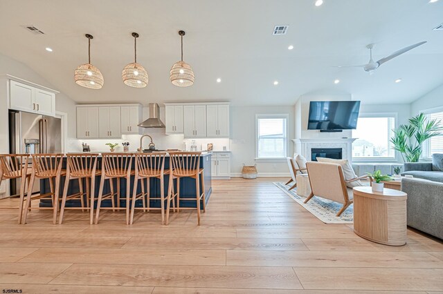 kitchen with high end fridge, open floor plan, wall chimney exhaust hood, light wood-style flooring, and vaulted ceiling