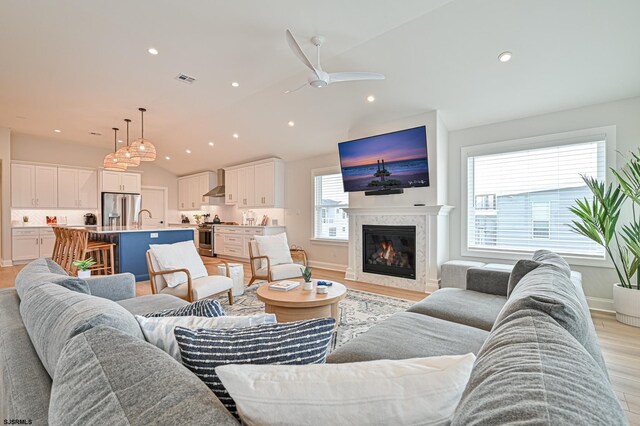 living area with light wood finished floors, a premium fireplace, a ceiling fan, baseboards, and lofted ceiling