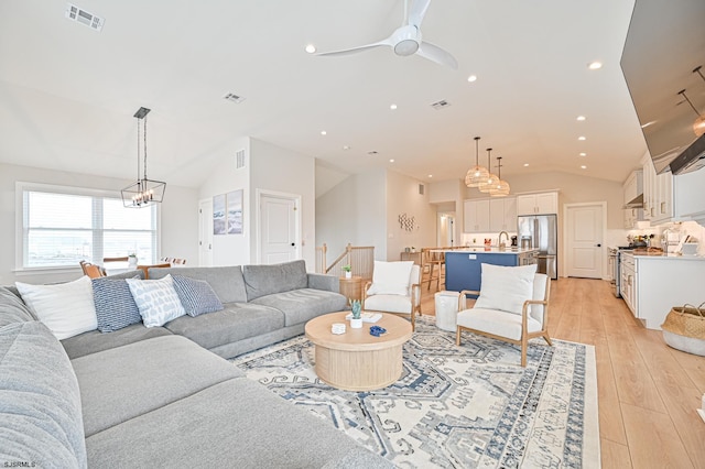 living area featuring vaulted ceiling, light wood-type flooring, visible vents, and ceiling fan with notable chandelier