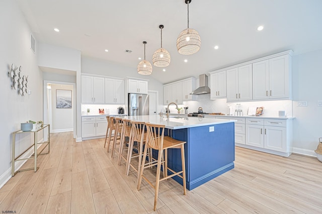 kitchen featuring a sink, stainless steel fridge with ice dispenser, light wood-style floors, wall chimney exhaust hood, and a spacious island
